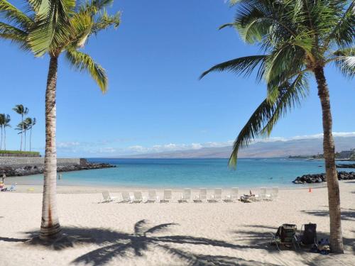 a beach with palm trees and chairs and the ocean at HAWAIIANA ESCAPE Tropical 3BR Kulalani Home with Bikes and Beach Club in Waikoloa