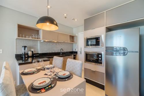 a kitchen with a table and a stainless steel refrigerator at MHF II - Apts Variados em Prédio com Vista para o Mar em Itapema in Itapema