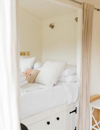 a bedroom with white walls and a bed with white pillows at Lapwing Hut in Cholderton