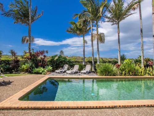 a swimming pool with two chairs and palm trees at Sunrise Cove 12 in Kingscliff