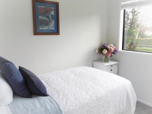 a white bedroom with a bed and a vase of flowers at The Gate House in Tauranga