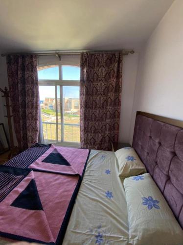 a bed in a room with a large window at Blumar El sokhna in Al Ḩafāʼir