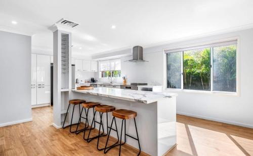 a white kitchen with stools at a counter at Cheerful 4-bedroom family retreat in Caves Beach in Caves Beach