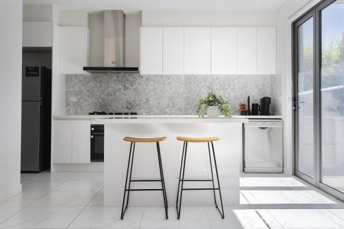 a kitchen with white cabinets and two bar stools at Modern Townhouse - Cafes, Shops, Bus, Freeway access in Balwyn North