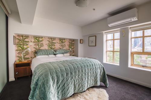 a bedroom with a bed with a green comforter and two windows at Deco Loft on Russell Street in Melbourne