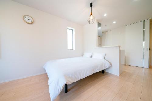 a white bedroom with a bed with a clock on the wall at Simple Stay Minoshima セルフチェックイン in Fukuoka