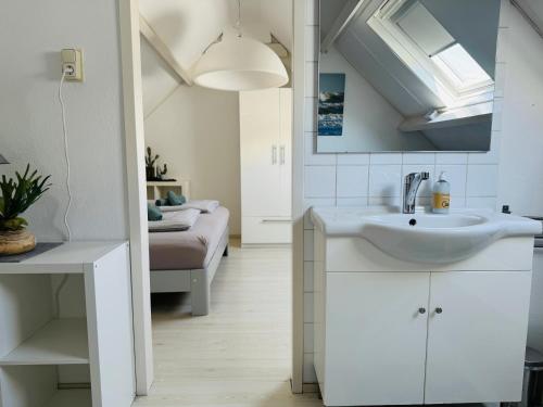 a white bathroom with a sink and a bedroom at Zomerhuis Rita in Egmond aan Zee