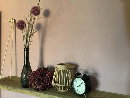 a shelf with a vase and a clock and flowers at Ferienwohnung Hümmling in Börger