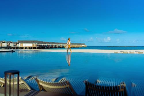 a woman walking on the beach next to a swimming pool at RAAYA By Atmosphere - Premium All Inclusive with Free Transfers in Raa Atoll