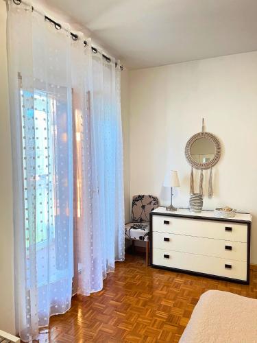 a bedroom with white curtains and a dresser and a mirror at La casa di Bianca - Casa Vacanze in Villa Opicina