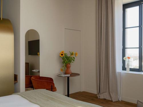a bedroom with a bed and a table with a vase of flowers at Hôtel Fort St Laurent Lyon - Handwritten Collection in Lyon