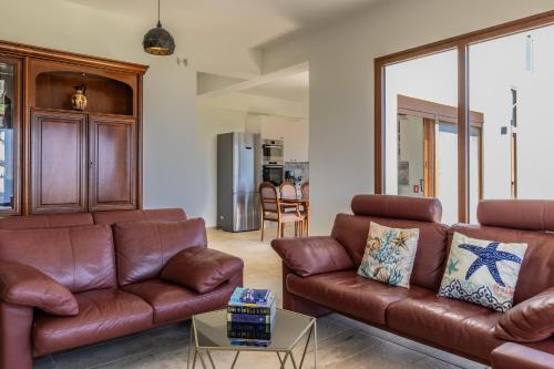 a living room with brown leather couches and a table at Beachfront Villa Atalandia with Heated Pool, Gym, BBQ & Office in Goúdhouros