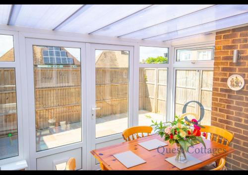 a conservatory with a wooden table with flowers on it at Pittlesden Cottage - Sleeps 4 - Tenterden in Tenterden