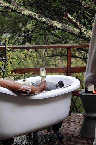 a person sitting in a bath tub with a glass of wine at Barefoot Addo Elephant Lodge in Addo