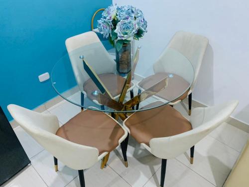 een glazen tafel met vier stoelen en een vaas met bloemen bij Apartamento Acogedor in San Felipe de Puerto Plata