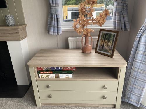 a wooden dresser with a vase and books on it at Bluebell Lodge at The Peaceful Cherry Lea Holiday Park and Fishing Lake Skegness in Skegness