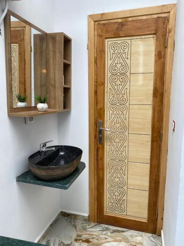 a bathroom with a sink and a wooden door at Appartement Les Vagues Bleues in Monastir