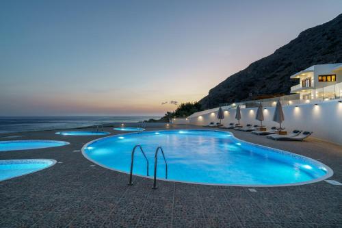 a row of swimming pools with umbrellas and the ocean at Beachfront Villa Atalandia with Heated Pool, Gym, BBQ & Office in Goúdhouros