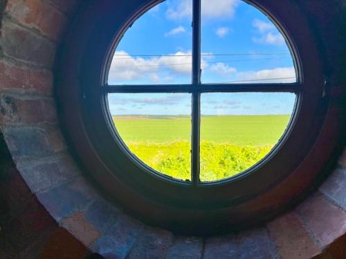 a round window with a view of a field of flowers at DRIFTWOOD - Super 1 Bedroom Home with Sea Views in Saint Levan