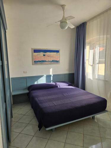 ein Schlafzimmer mit einem Bett mit lila Laken und einem Deckenventilator in der Unterkunft Casa prima fila con Vista Mare in Isola Rossa