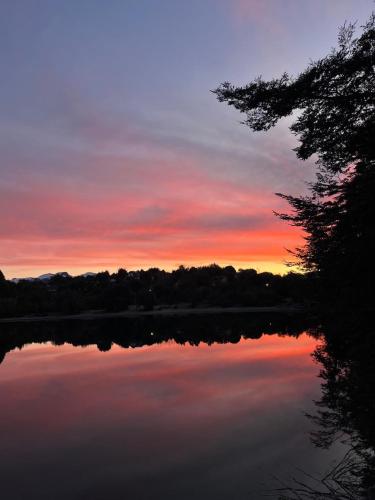a sunset over a lake with trees in the background at Costa de Lago - Cullelafquen in Villa Pehuenia