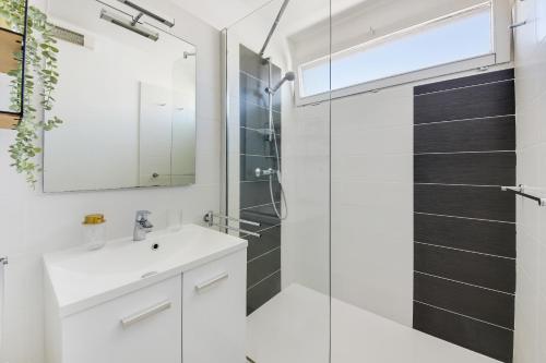 La salle de bains est pourvue d'un lavabo blanc et d'une douche en verre. dans l'établissement La Perle - Vue Mer, Parking Privée Clos, Traversant ,Tv 4K, Fibre, à Canet