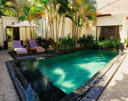 a swimming pool in front of a house with palm trees at BrightUp Villa Beach Side Sanur in Sanur