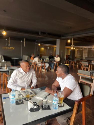 two men sitting at a table in a restaurant at Royal Hotel Apartments in Kampala