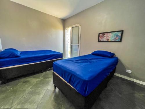 a bedroom with two beds with blue sheets and a window at 04 · No Fresquinho do Ar in Guarujá