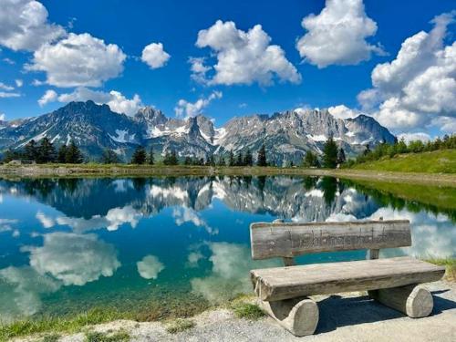 a bench sitting in front of a lake with mountains at Dreilärchenhaus in Brixen im Thale