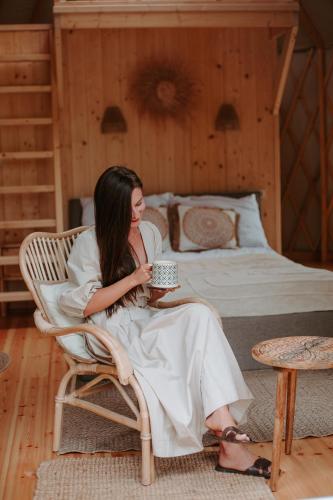 a woman sitting in a chair holding a cup of coffee at Jurta w Dolinie Sanu in Krzemienna