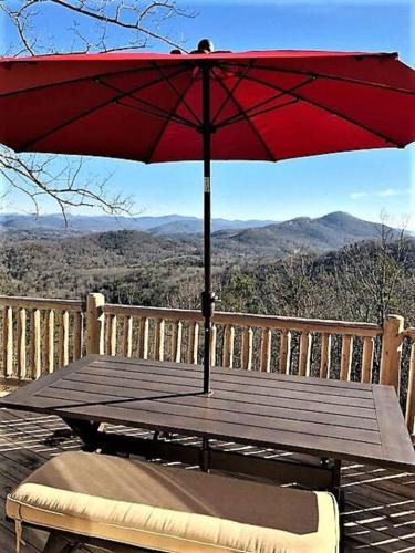 a picnic table with a red umbrella on a deck at Ultimate Log Cabin Experience with BREATHTAKING Views in Yonah