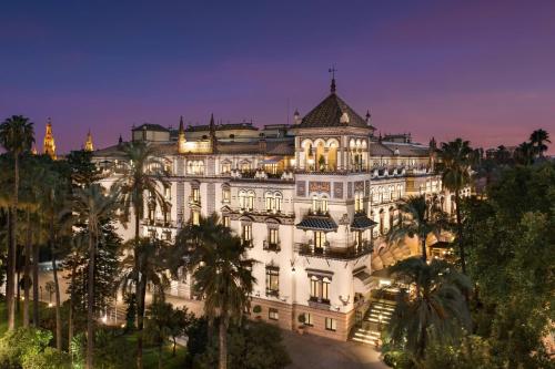 un grand bâtiment blanc avec des palmiers la nuit dans l'établissement Hotel Alfonso XIII, a Luxury Collection Hotel, Seville, à Séville