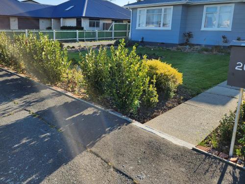 a driveway with bushes and a house with a sign at Minimalist Cabin Solo Traveller in Ashburton