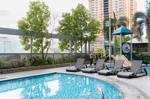 a swimming pool with lounge chairs next to a building at Cubao Manhattan Heights Residential Condo TB30N - High Floor Studio with Balcony City View, Pool, Netflix, 5-Min Walk to the Araneta Coliseum Gateway Mall SM - Staycations by SMS in Manila