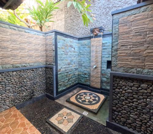 a bathroom with a shower with a stone wall at Suka Sari Cottages in Pemuteran