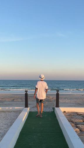 a man standing on the beach looking at the ocean at bh villa in Al Ashkharah