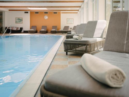 a pool with lounge chairs next to a swimming pool at Hotel Vitalquelle Montafon in Schruns-Tschagguns