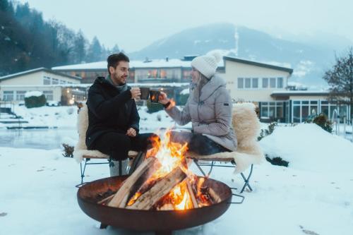 a man and woman taking a picture next to a fire at Hotel Vitalquelle Montafon in Schruns-Tschagguns