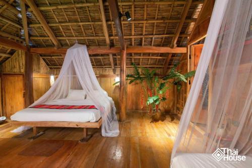 a bedroom with a bed with a mosquito net at Thai House Pu Luong - Century Old Stilt House with Terrace Views in Hương Bá Thước