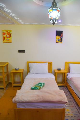 two beds in a room with two tables and a lamp at Hotel De La Vallée in Aït Baha