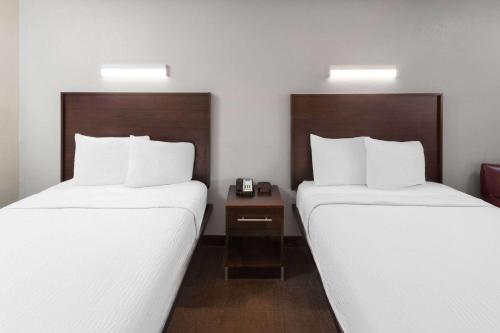 two beds in a hotel room with white sheets at Travelodge by Wyndham Peoria in Peoria
