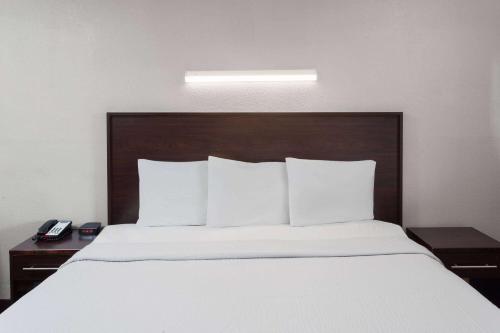 a large bed with white sheets and a wooden headboard at Travelodge by Wyndham Peoria in Peoria