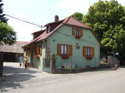 a small green house with red shutters on a street at Gîte des Hirondelles in Issenheim