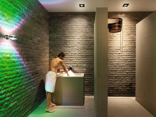 a man standing in a bathroom with a sink at Dolomitengolf Hotel & Spa in Lavant