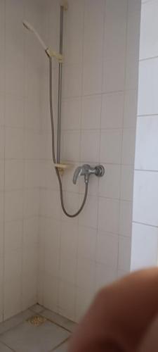 a shower in a white tiled bathroom with a hose at Central apartman in Nivy