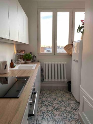 - une cuisine avec des placards blancs, un évier et 2 fenêtres dans l'établissement Charmant Appartement Typique Parisien, à Paris