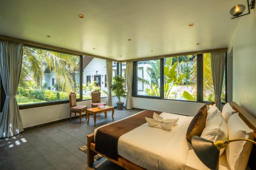 a bedroom with a large bed and large windows at Regenta Resort Mysore Tropical Village in Chāmundi