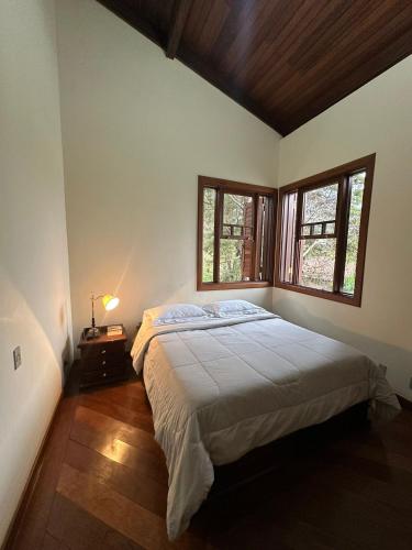 a bedroom with a large bed and two windows at Temporada Retiro do Chalé Brumadinho MG in Brumadinho