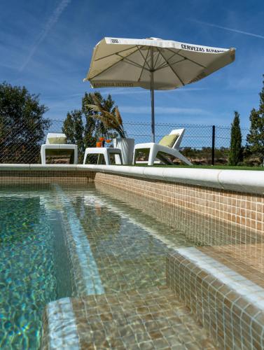 a swimming pool with an umbrella and chairs and a table at Casa Rural La Yesería Alcocer in Sacedón
